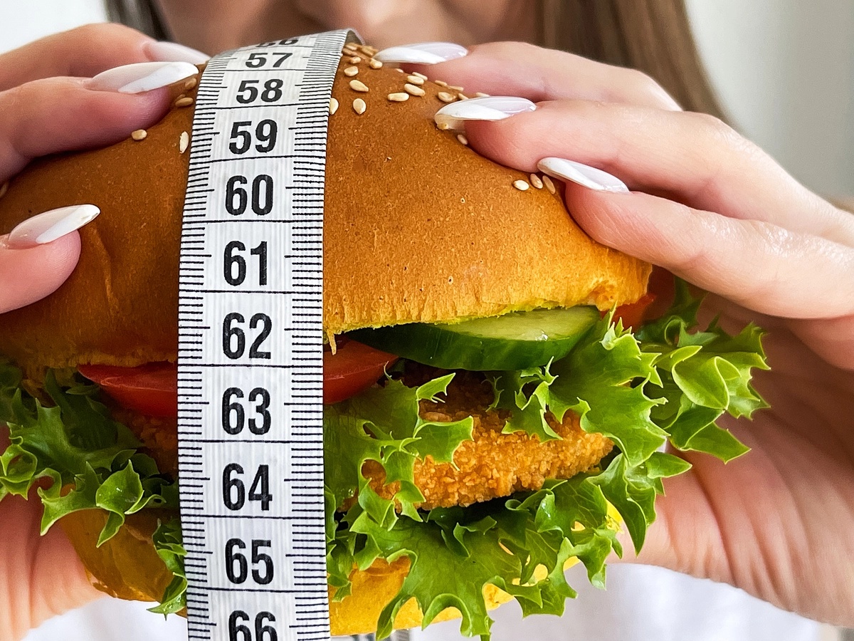 A large hamburger with a tape measure wrapped around it.