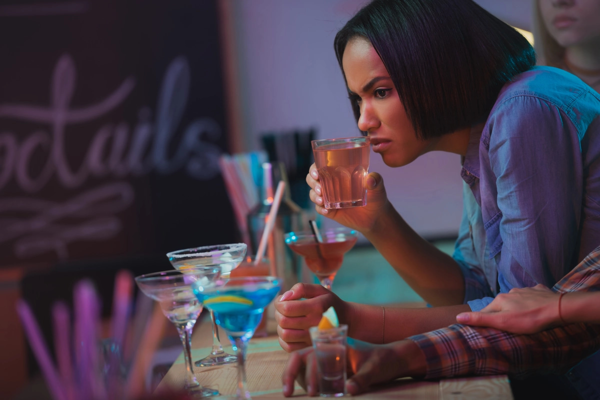 A woman at a bar sipping on a mixed drink, potentially fueling an underlying mental health disorder with an addiction.