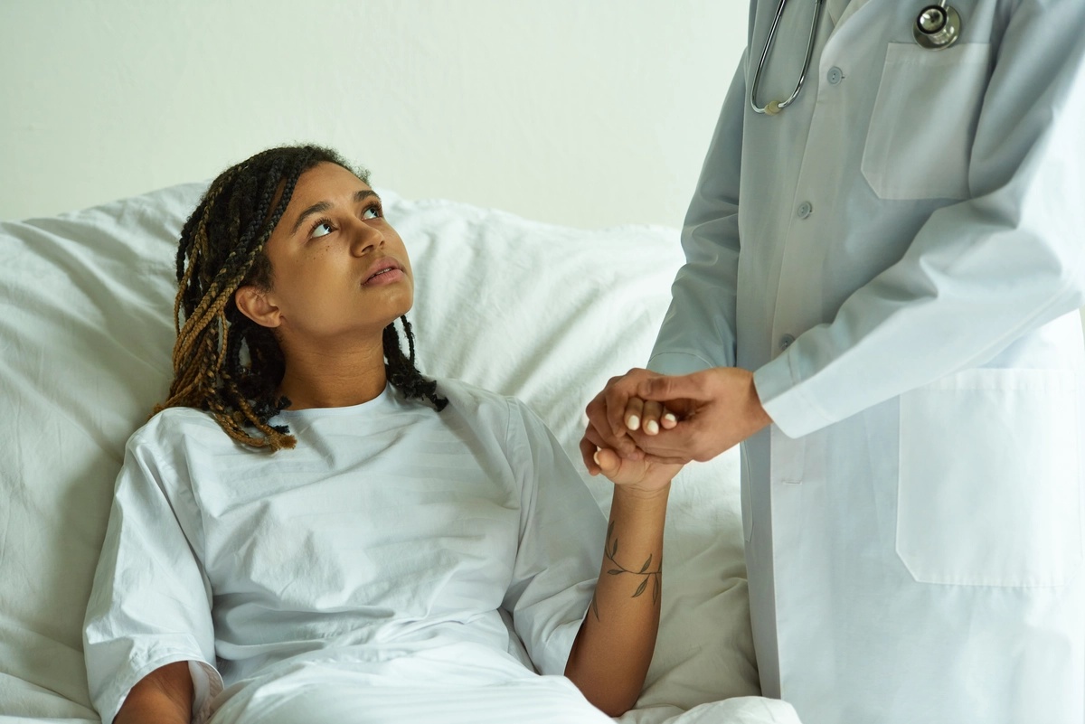 An inpatient woman in a hospital bed being comforted by her doctor.