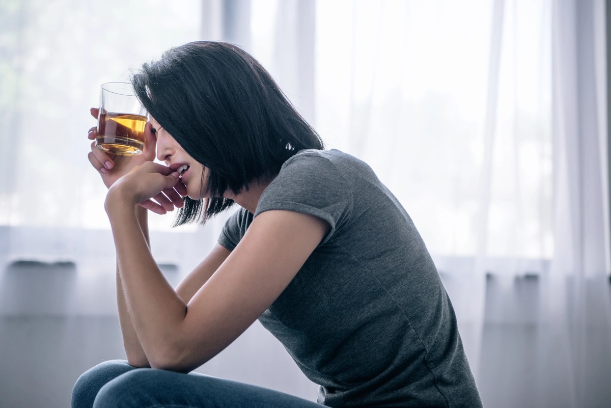 A woman crying as she holds a glass of whiskey to her head, possibly struggling with alcohol addiction.