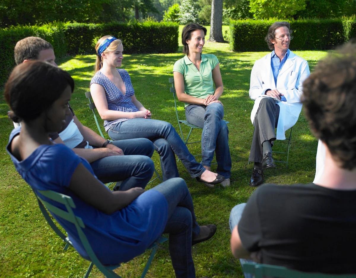 A drug rehab group therapy session is being held outside in a garden.