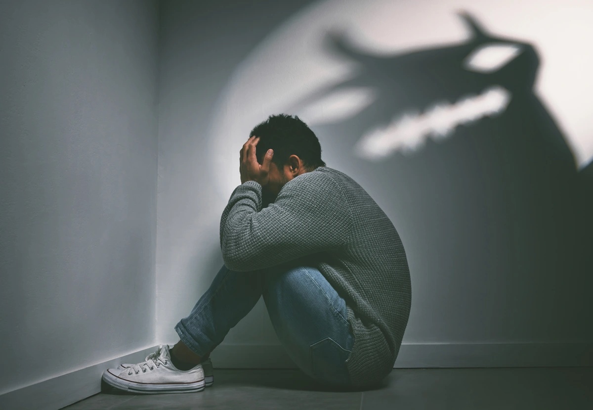 A man sitting in the corner is menaced by the shadows.