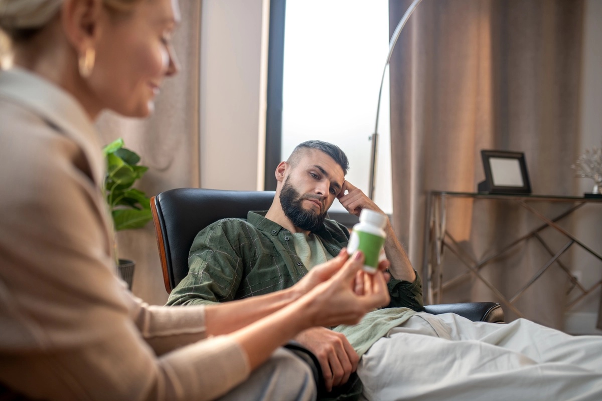 A therapist holds a pill bottle while speaking to an outpatient rehab client.