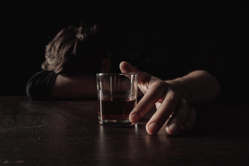 Photo of a man with his head down at a bar, a drink near his hand.