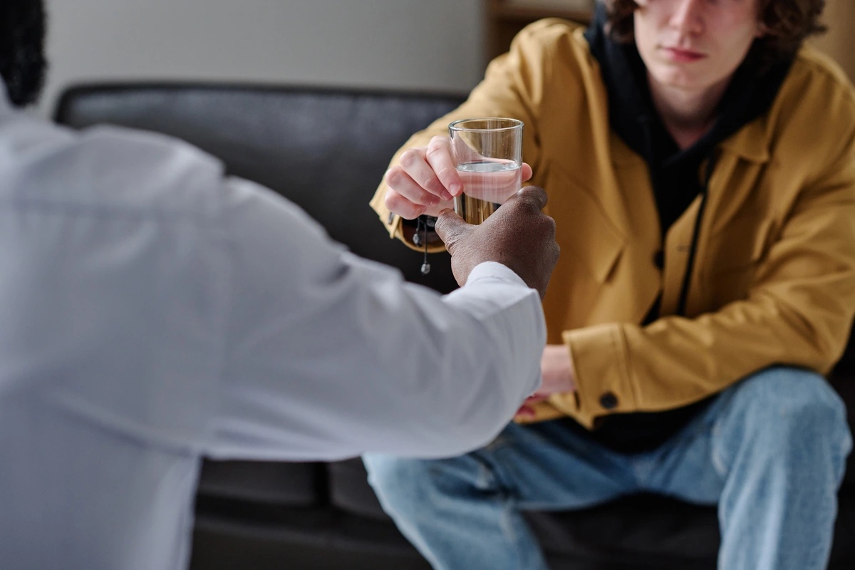 During an alcohol rehab therapy session, a doctor hands his patient a glass of water.