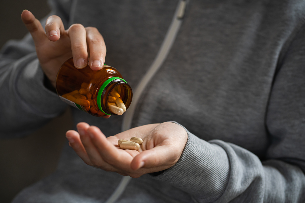A man places opioid pills into his hand, a possible sign of opioid addiction.