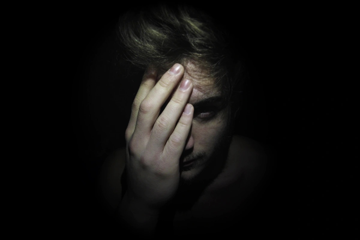 A man suffering from simple schizophrenia in a dark room holding his hand over his eye.