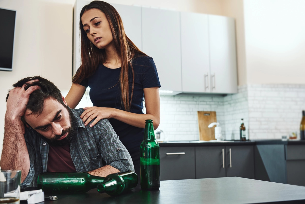 A woman comforts a man, who is likely struggling with alcohol addiction.