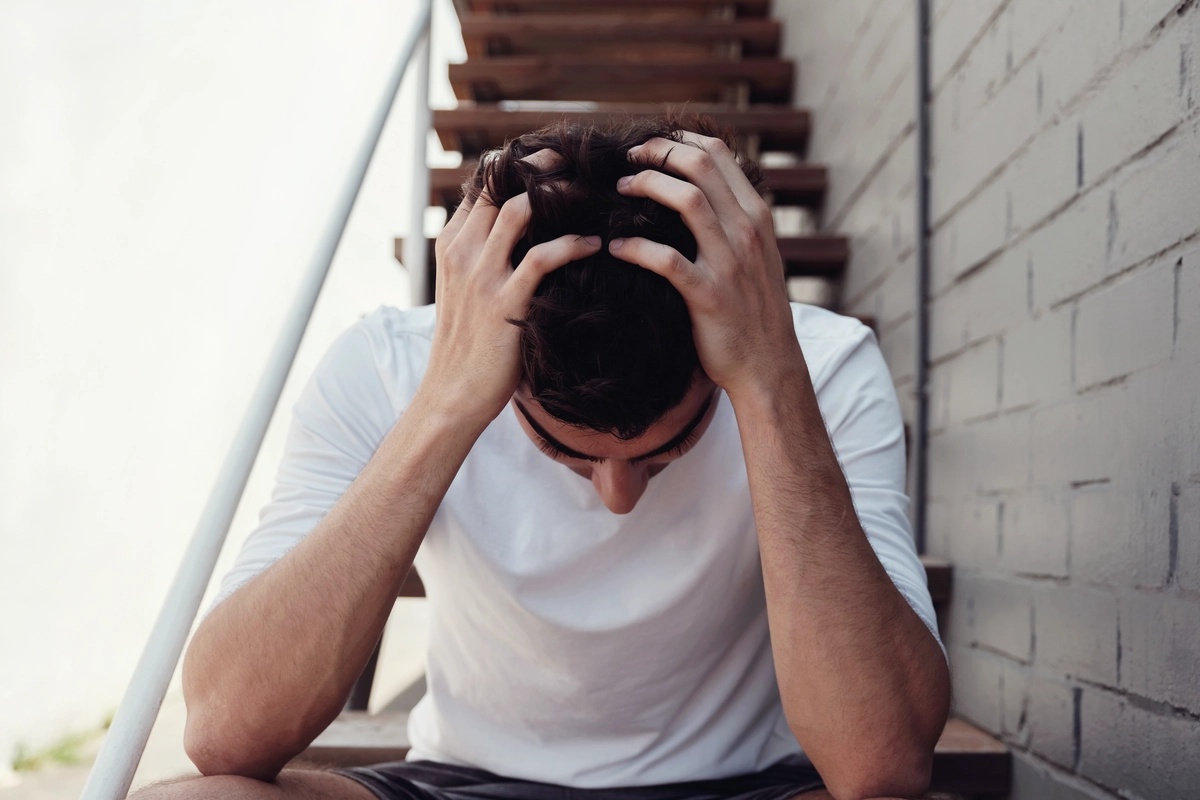 A man struggling with simple schizophrenia sitting on a staircase with his head in his hands battling the signs of simple schizophrenia.