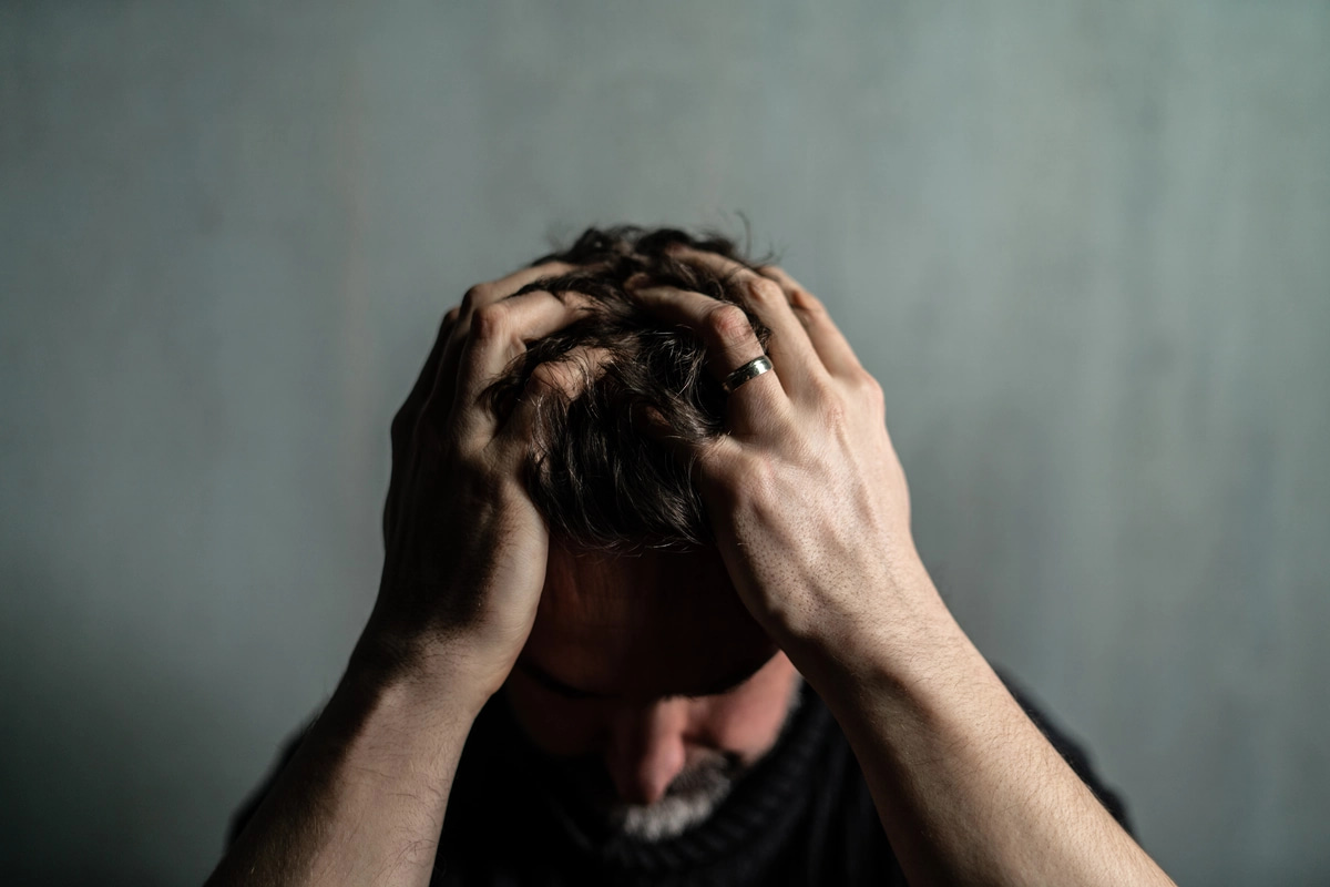 A person struggling with prescription drug addiction poses with their hands pressed to their head.