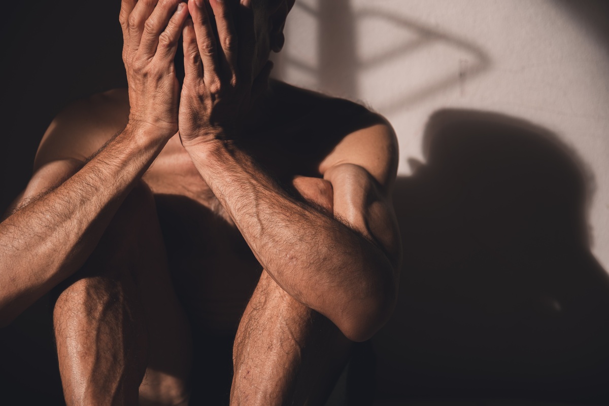 A man with his knees to his chest holding his face in his hands.