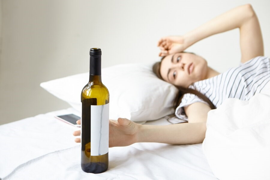 Photo of a young woman in bed with a wine bottle