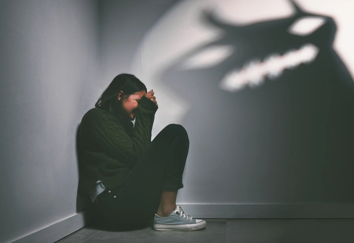 A woman crouches in the corner, menaced by a shadow.