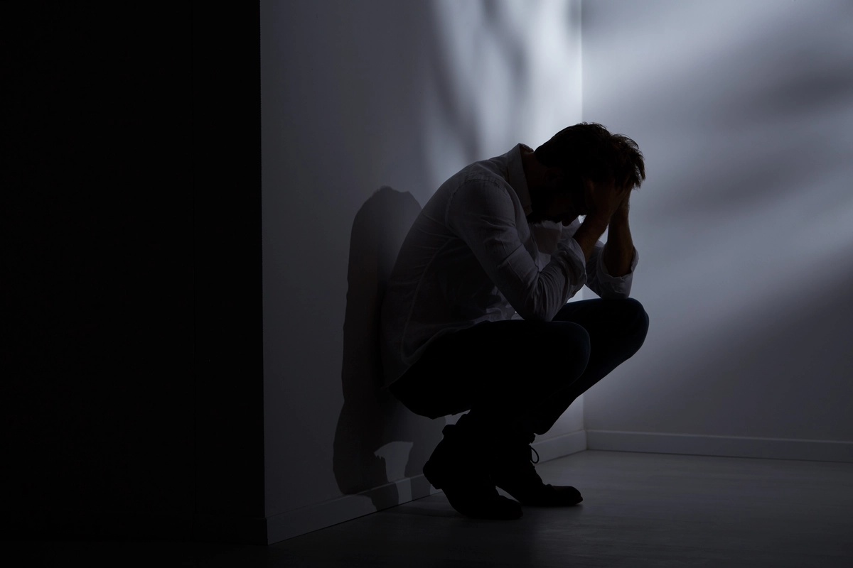 A man crouched against a wall with his head in his hands