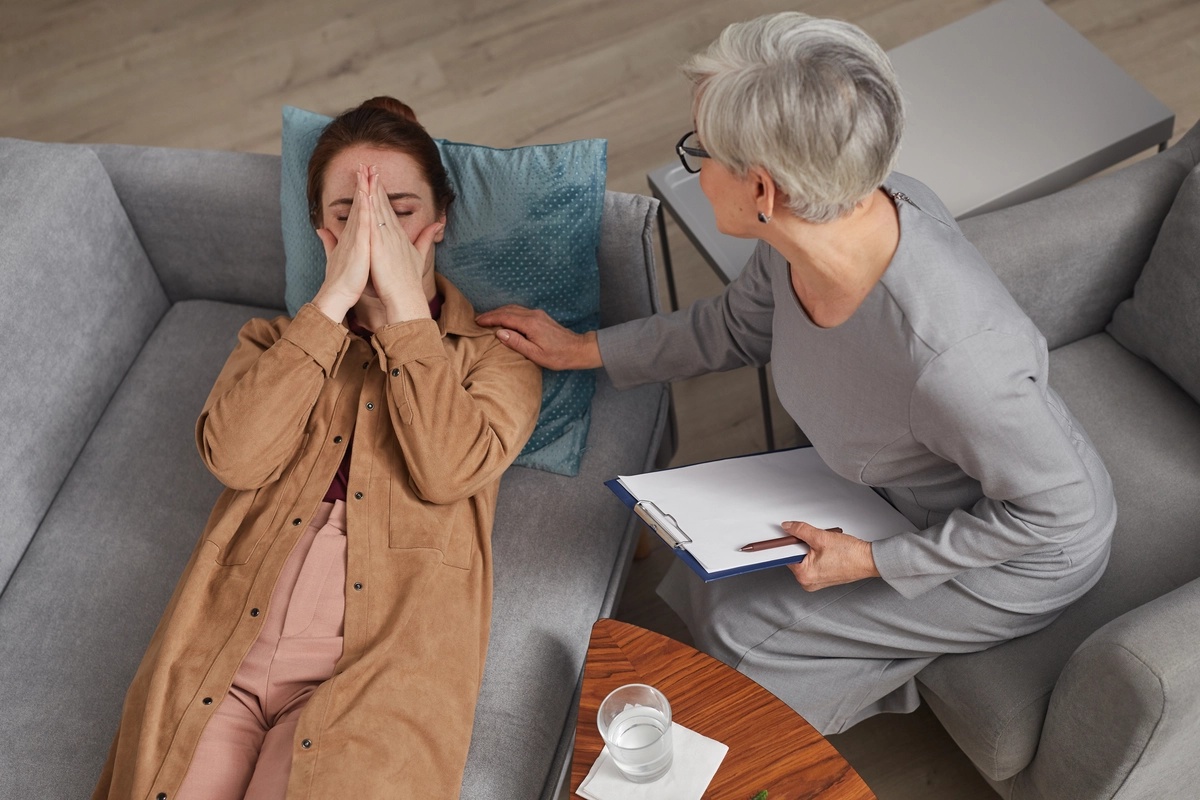 A woman undergoing crisis stabilization lying on a couch is being comforted by a therapist. A woman undergoing crisis stabilization lying on a couch is being comforted by a therapist.