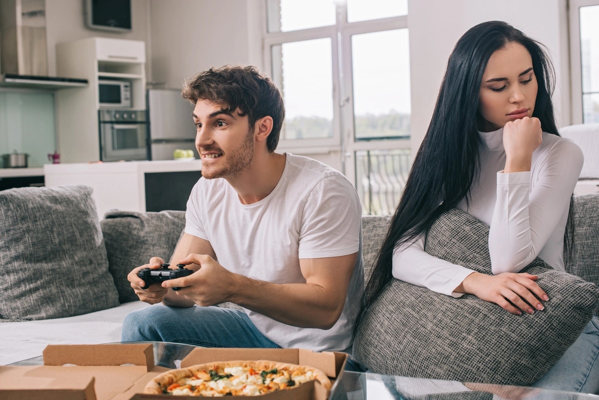 A man with a video game addiction, playing video games while his partner sits in frustration. A man with a video game addiction, playing video games while his partner sits in frustration.