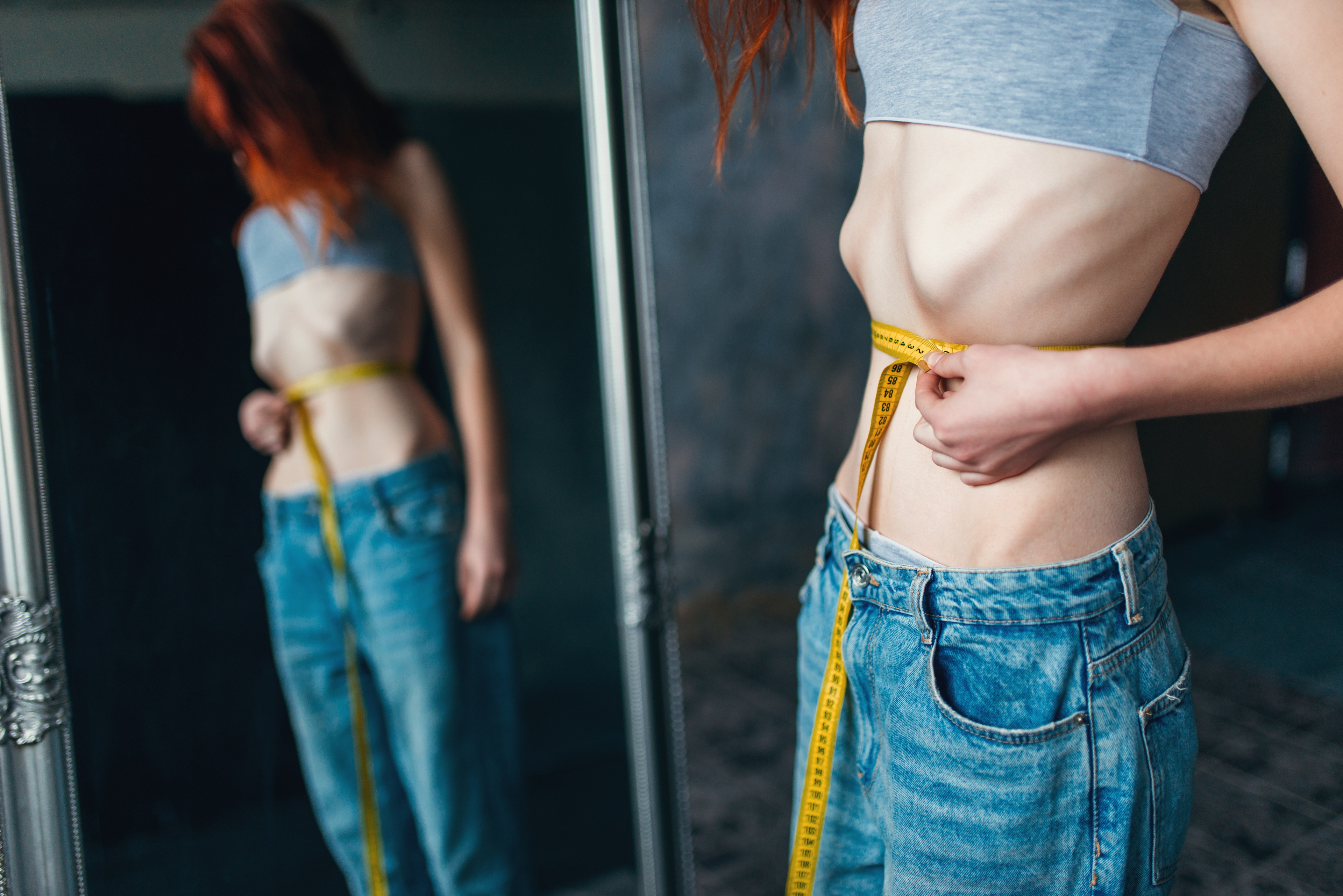 woman-measures-waist-against-mirror-weight-loss-2024-11-28-15-35-21-utc
