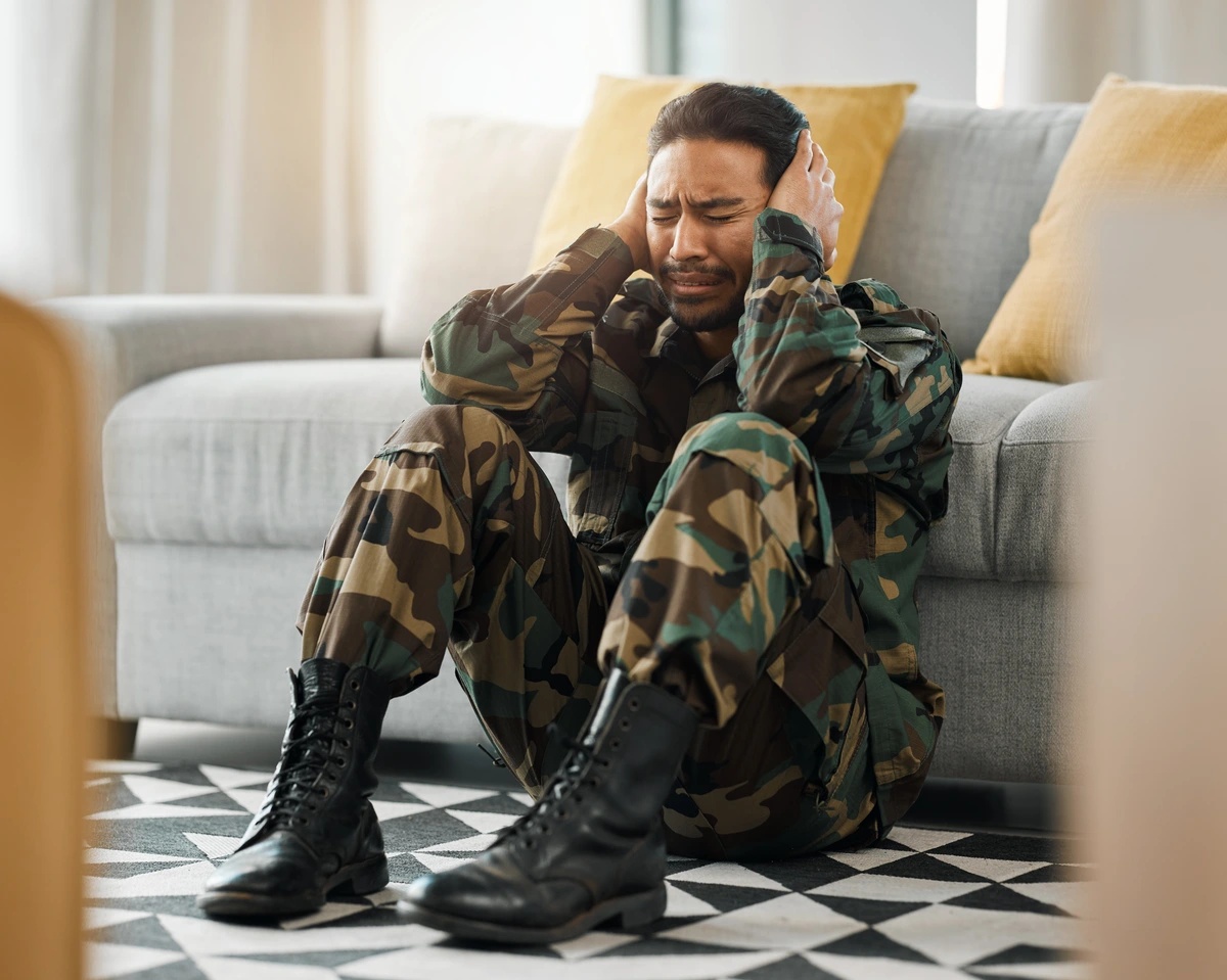 PTSD: Post-Traumatic Stress Disorder A man in camouflage sits on the floor in front of a sofa, suffering.