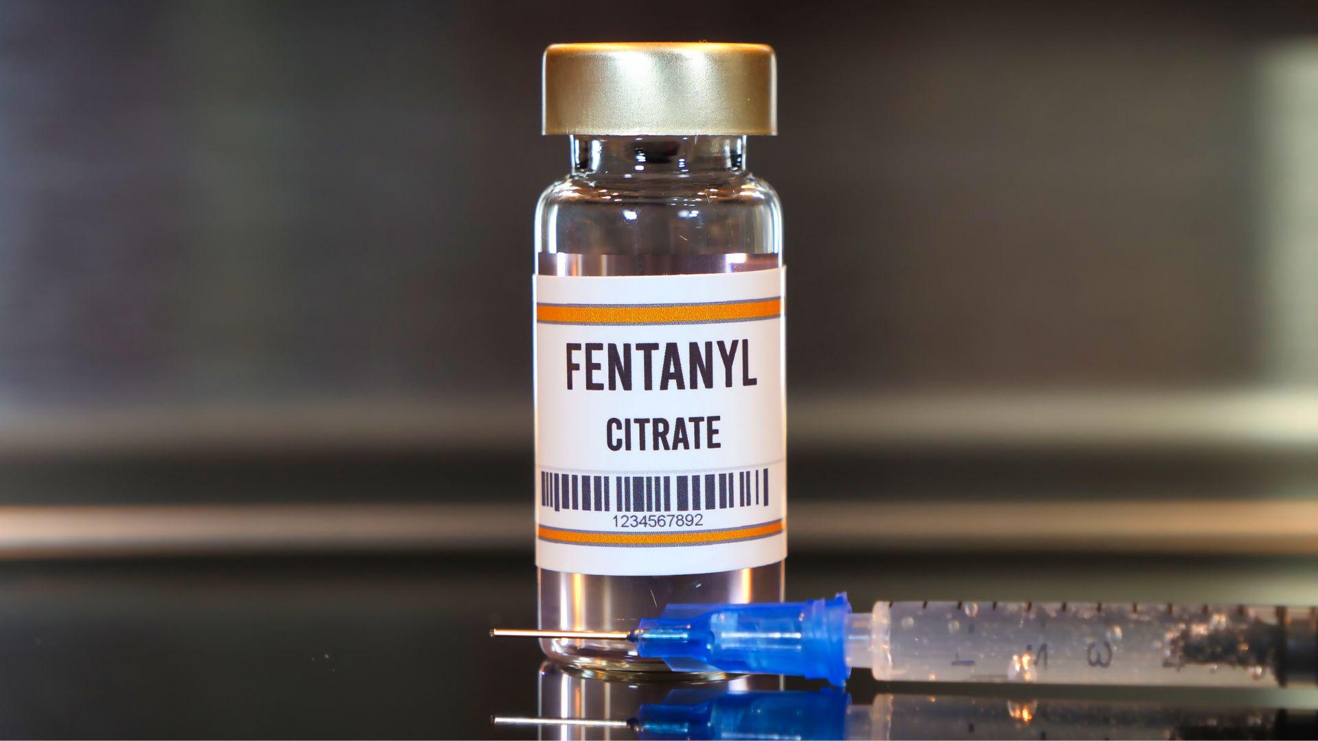Fentanyl drug and syringe on black table with reflections and stainless background