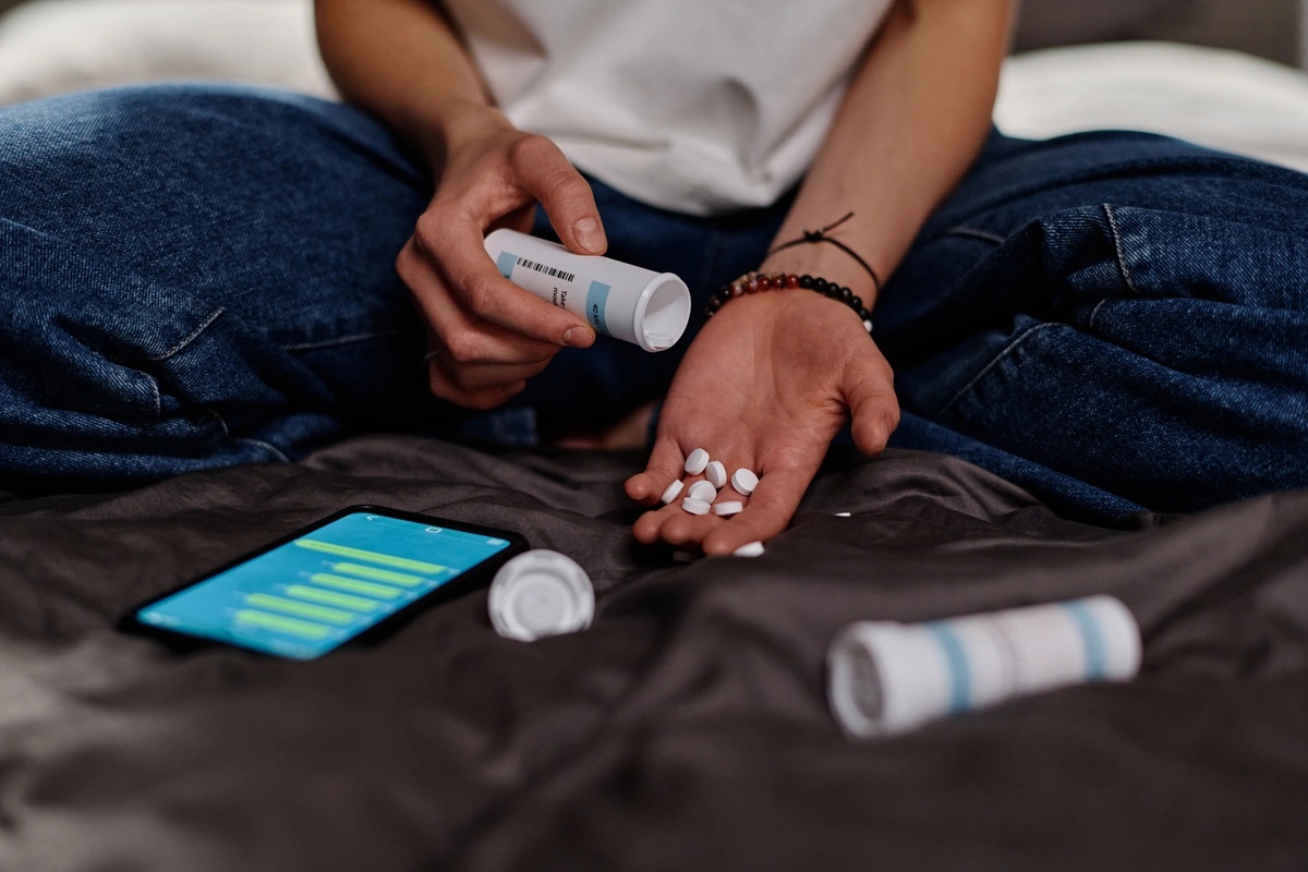 A person sitting with a bottle of Xanax in one hand and a handful of pills in the other, struggling with Xanax addiction. A person sitting with a bottle of Xanax in one hand and a handful of pills in the other, struggling with Xanax addiction.