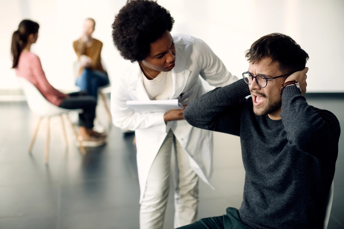 A man struggling to manage painful memories while in trauma-informed therapy, with a therapist comforting him.